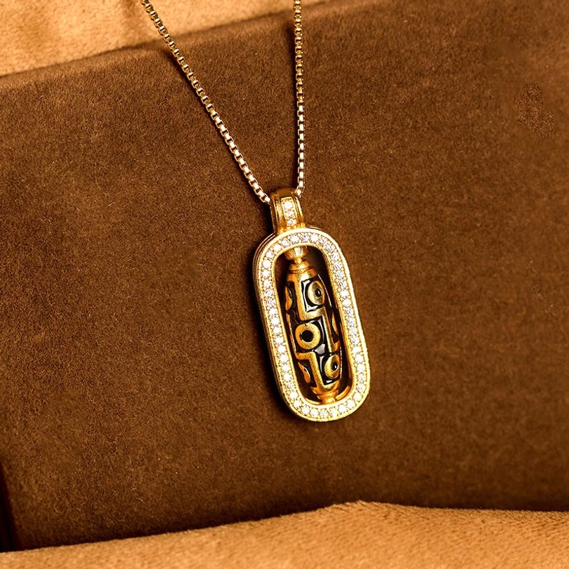 Polished nine-eye dzi bead pendant on brown suede fabric background, overhead front close-up showing zircon halo trim