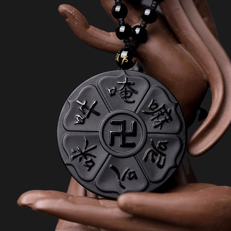 Black obsidian Tibetan Buddhist pendant necklace with swastika and six-syllable mantra, held by Buddha statue hand, angled view