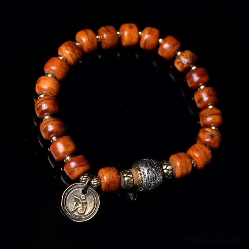 Tibetan OM bracelet top-down view with reddish camel bone beads and engraved metal OM charm on black background