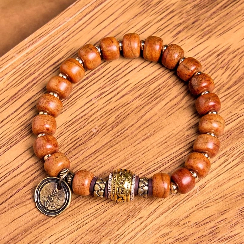 Top-down view of Tibetan luck protection bracelet featuring uniform camel bone beads with metal spacer and stamped OM charm on wood grain