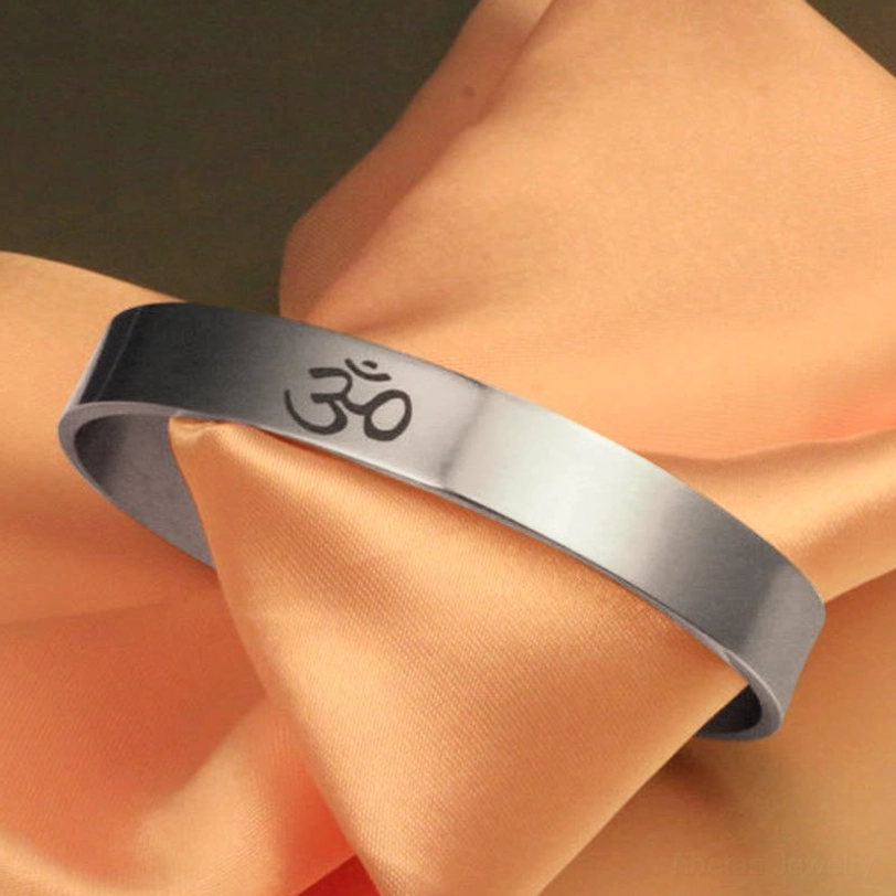 Tibetan OM symbol engraved open cuff bracelet in polished silver titanium steel, adjustable design displayed on peach satin fabric