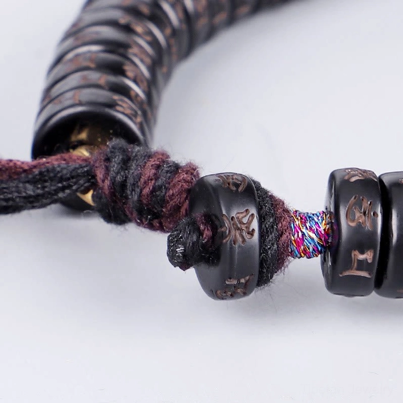 Full front flat lay view of complete Tibetan om mani padme hum bracelet showing disc-shaped coconut beads with mantras and fabric tassel