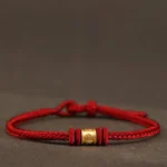 Tibetan Om Mani Padme Hum red string bracelet with 999 gold engraved charm, flat lay view on dark background