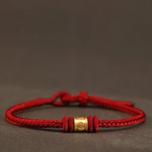 Tibetan Om Mani Padme Hum red string bracelet with 999 gold engraved charm, flat lay view on dark background