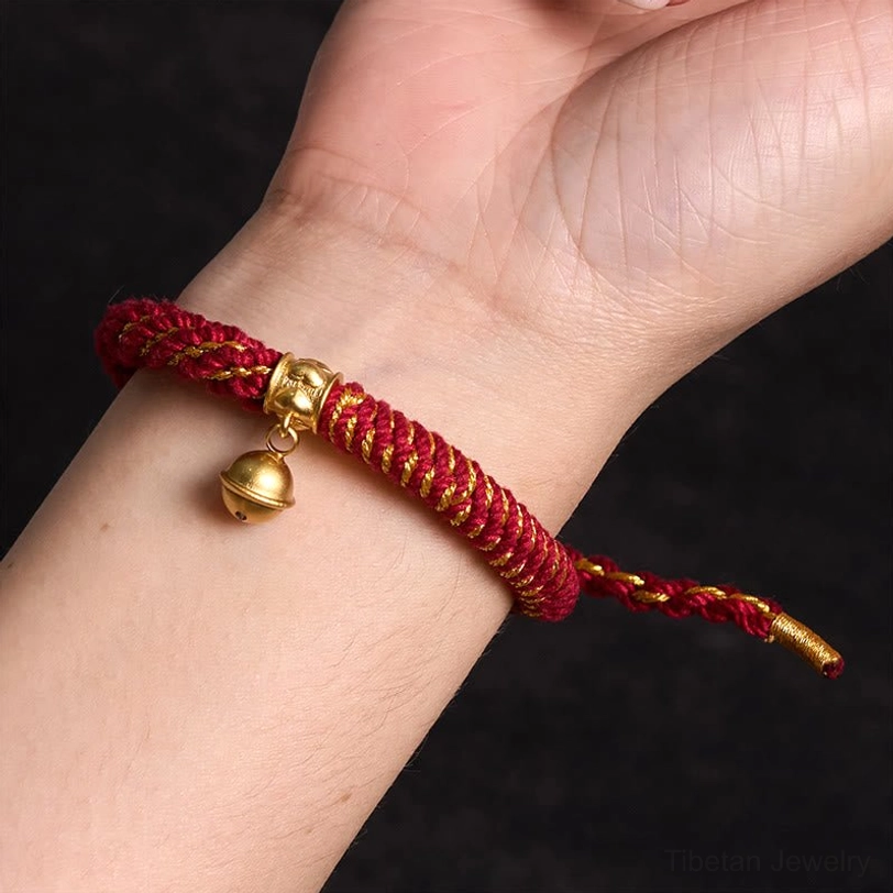 Adjustable Tibetan mantra bracelet featuring engraved sacred symbols and brass bell pendant on natural stone background