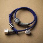 Tibetan Om Mani Padme Hum double wrap rope bracelet with royal blue braided cord and silver engraved amulet charms on tan background, top-down flat lay view