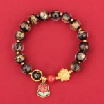 Tibetan Om Mani Padme Hum Liuli glass bracelet with spotted black beads, gold lotus charm, and Fu character enamel pendant on red background