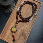 Tibetan Om Mani Padme Hum wood bead necklace with copper enamel pendant displayed on wooden tray