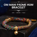 Multicolored Tibetan Om Mani Padme Hum bracelet with gold metal accents and brass bell charm, displayed on dark stone surface with blue fabric