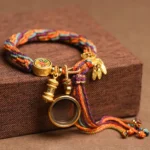 Tibetan Om Mani Padme Hum protection bracelet with multicolor braided rope and gold metal charms displayed on wooden surface