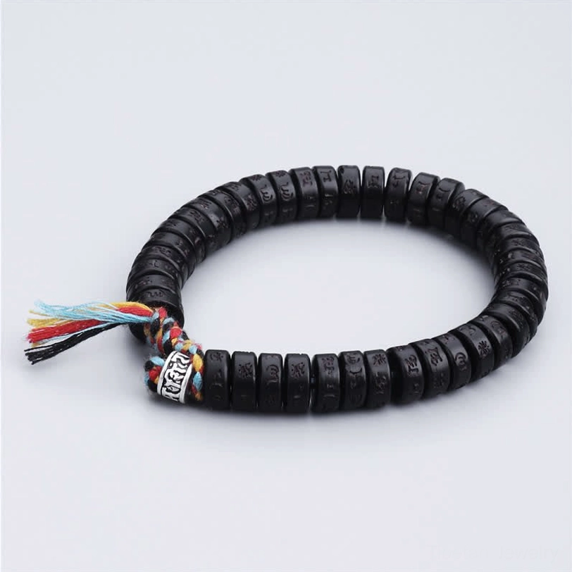 Handmade Tibetan Om Mani Padme Hum bracelet three-quarter view featuring flat black coconut shell beads, silver engraved accent bead, and colorful tassel