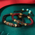 Tibetan Om Mani Padme Hum braided bracelet in wine red and dark brown rope with turquoise beads and gold copper fittings, flat lay on velvet backdrop