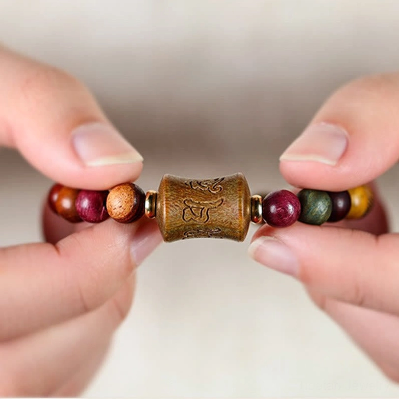 Close-up detail of Om Mani Padme Hum carved wooden bead held between fingers showing intricate mantra carving and natural wood texture