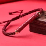 Handcrafted cinnabar Om Mani Padme Hum braided bracelet with gold-toned hardware, displayed on red backdrop