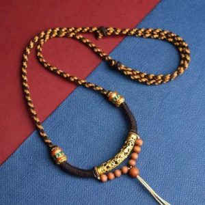 Tibetan handmade Om Mani Padme Hum prayer necklace with King Kong knot braided rope, gold tube, and wooden beads on red and blue fabric background