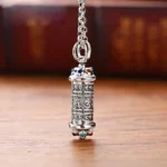 Tibetan Om Mani Padme Hum silver pendant necklace with engraved mantra script and colored gemstone accents, front view on wooden table