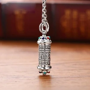 Tibetan Om Mani Padme Hum silver pendant necklace with engraved mantra script and colored gemstone accents, front view on wooden table