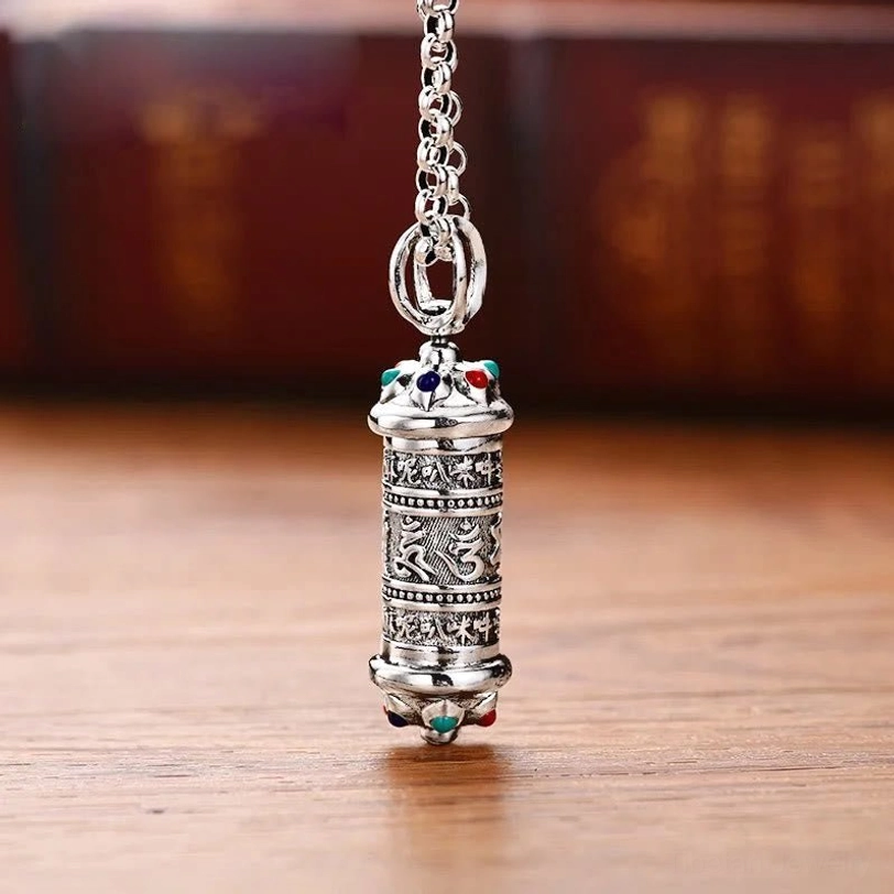 Tibetan Om Mani Padme Hum silver pendant necklace with engraved mantra script and colored gemstone accents, front view on wooden table
