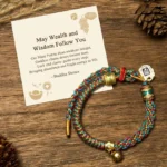 Om Mani Padme Hum Tibetan wealth bracelet with multicolored braided string and Zakiram goddess charm pendant displayed on wooden surface with natural decorations
