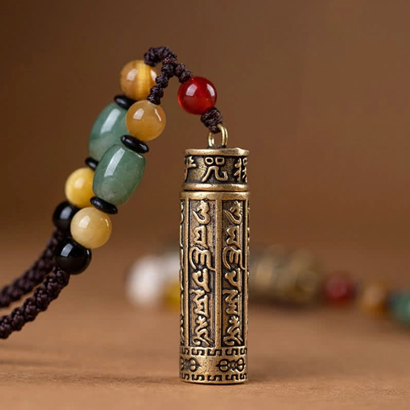 Detailed close-up of Tibetan pendant showing full engraved Om Mani Padme Hum sutra on brass cylinder with beaded hanging chain
