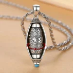 Tibetan Om Mani Padme Hum rotatable pendant necklace with 360-degree rotating inner core, vintage silver finish and blue gem detail on wooden surface
