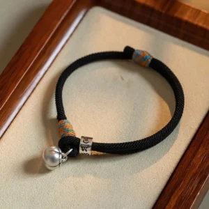 Black om mani padme hum persimmon charm bracelet with silver bell and engraved bead on velvet mat