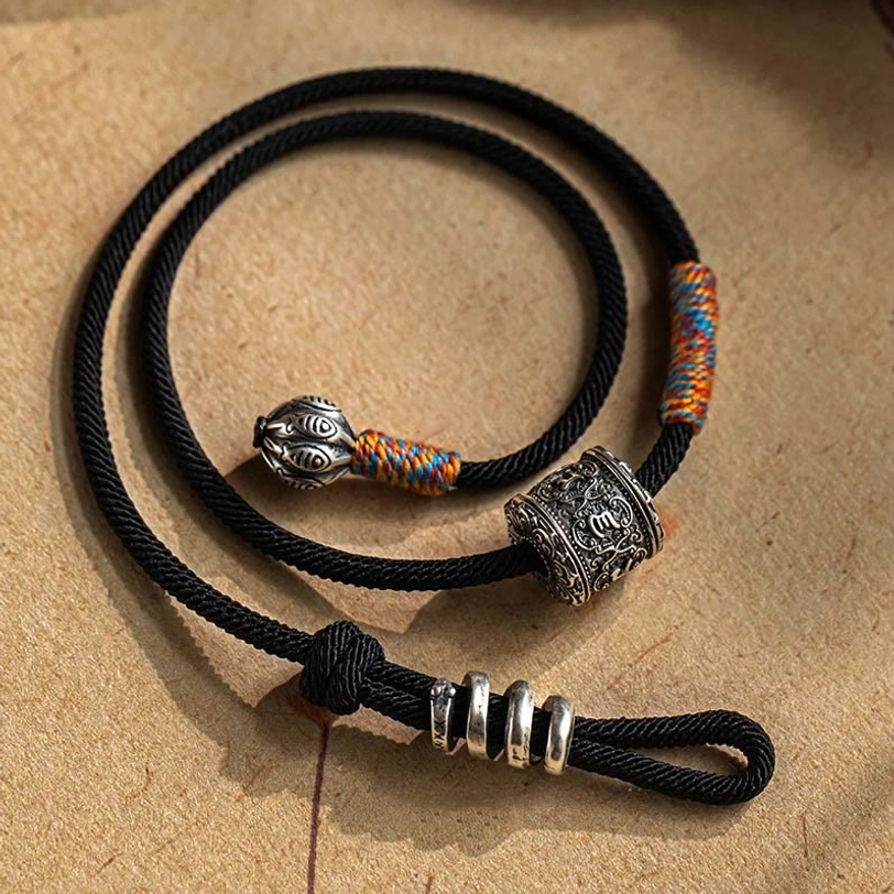 Tibetan amulet bracelet showing engraved double fish bell pendant and black braided cord design