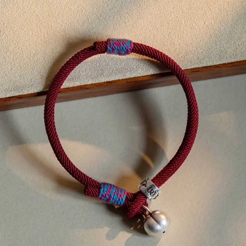 Wine red braided om mani padme hum persimmon charm bracelet with silver bell on wooden tray