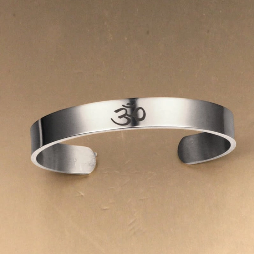 Direct front facing view of OM engraved open adjustable cuff bangle in polished silver titanium steel