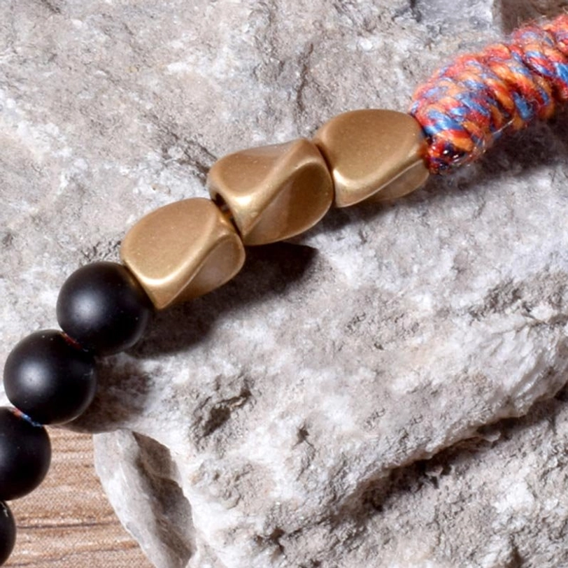 Extreme close-up of Tibetan black onyx tassel bracelet showing polished onyx beads, irregular gold metal accents, and colorful woven tassel