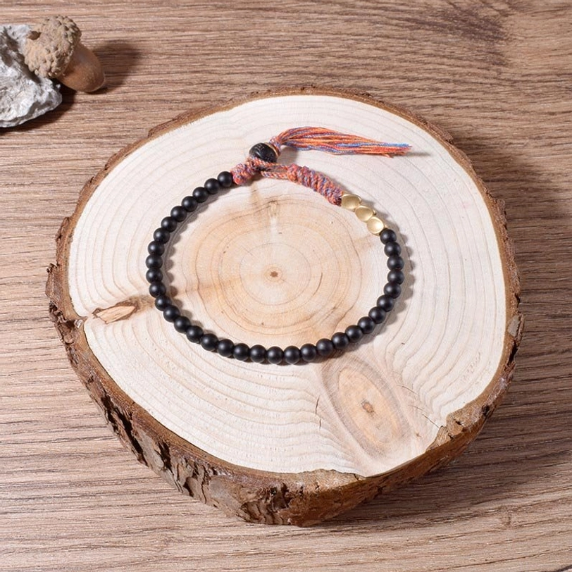 Authentic Tibetan black onyx bracelet with colorful braided tassel and gold metal accents displayed on wooden coaster