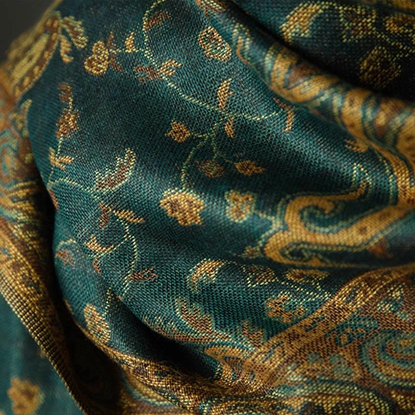 Macro photography of tibetan paisley scarf showing teal base texture with gold-brown woven floral pattern