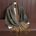 Tibetan jacquard paisley tassel shawl in dark green with brown decorative accents, displayed flat on leather sofa showing intricate woven pattern and frayed hem