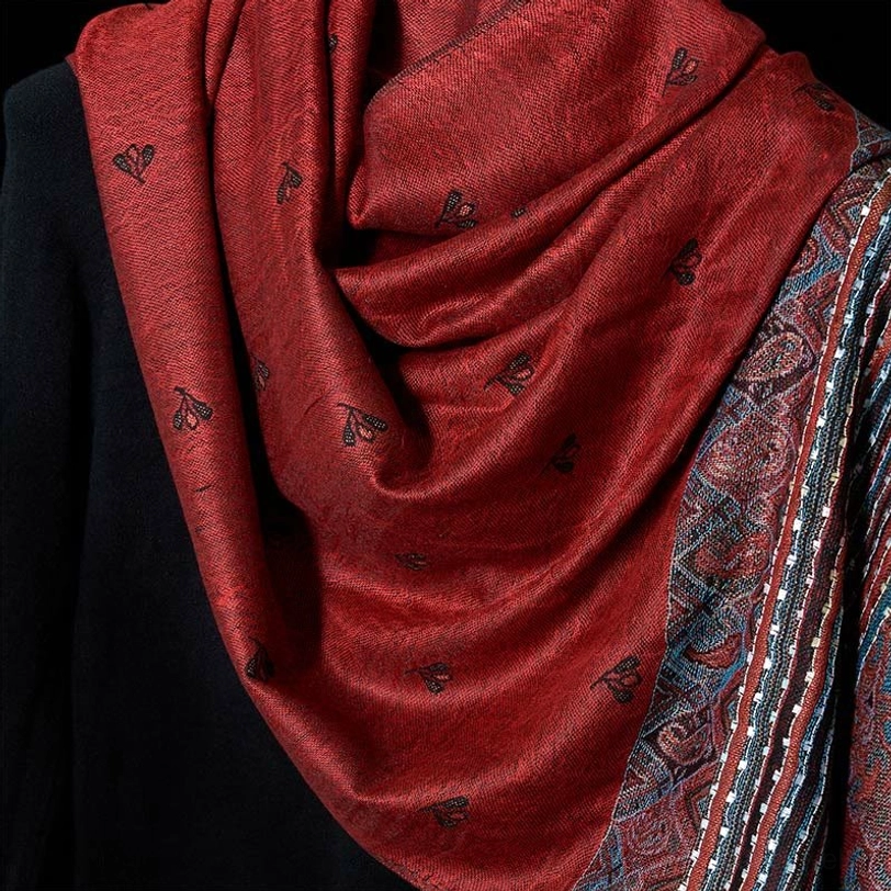 Close-up flat view of Tibetan paisley shawl fabric showing intricate tiny paisley motifs and geometric designs on red background, detail shot of weaving craftsmanship