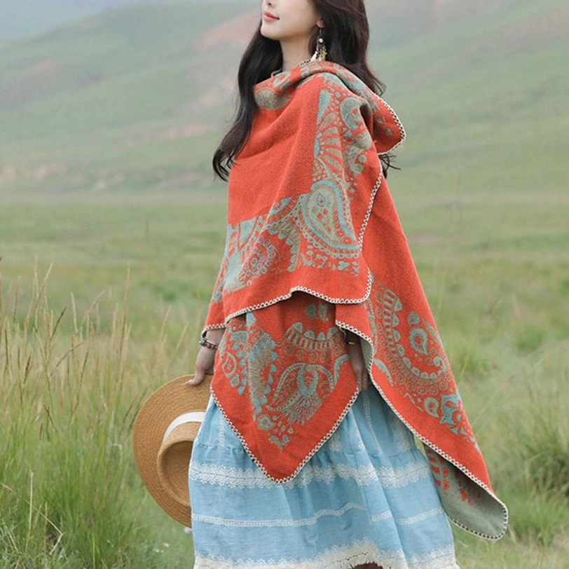 Tibetan paisley poncho shawl with beige stitched trim worn outdoors, three-quarter left side view on grassland