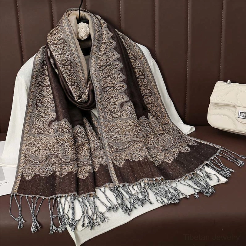 Grey-brown reversible paisley tassel scarf displayed on leather sofa showing long mixed-tone tassel edges and neutral palette