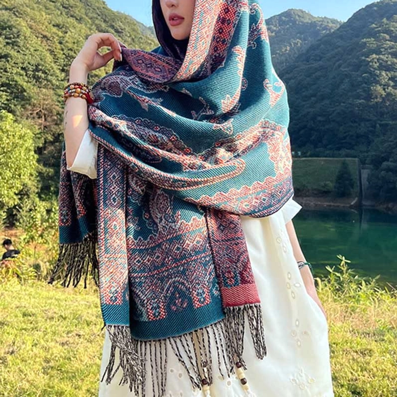 Side three-quarter view of blue and brown Tibetan paisley shawl with cream and red accents at lakeside mountain setting, draped style with tassel hem