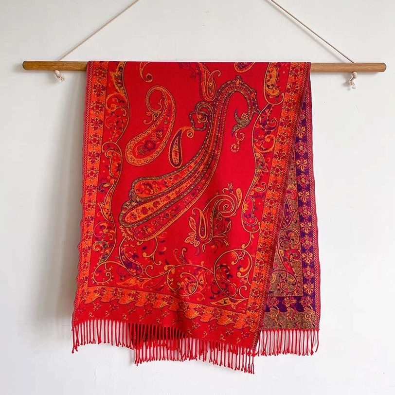 Bright red Tibetan paisley thermal shawl with orange and purple print, displayed on white wall backdrop