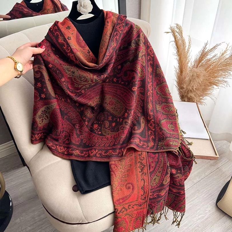 Hand holding burgundy orange Tibetan paisley shawl showing textured fabric and fringe