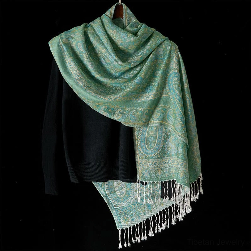 Soft teal Tibetan paisley shawl with white tassel fringe draped over shoulder, three-quarter styling view