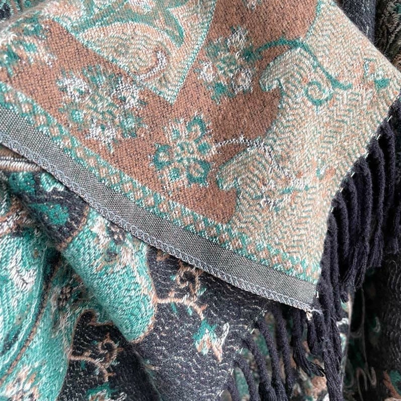 Flat lay detail shot of Tibetan tassel shawl showing woven jacquard texture, multi-color paisley design, and black fringe trim