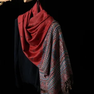 Tibetan paisley tassel shawl in FireBrick red with geometric stripe pattern, draped on black knit top - oblique hanging view showing solid color and patterned sections