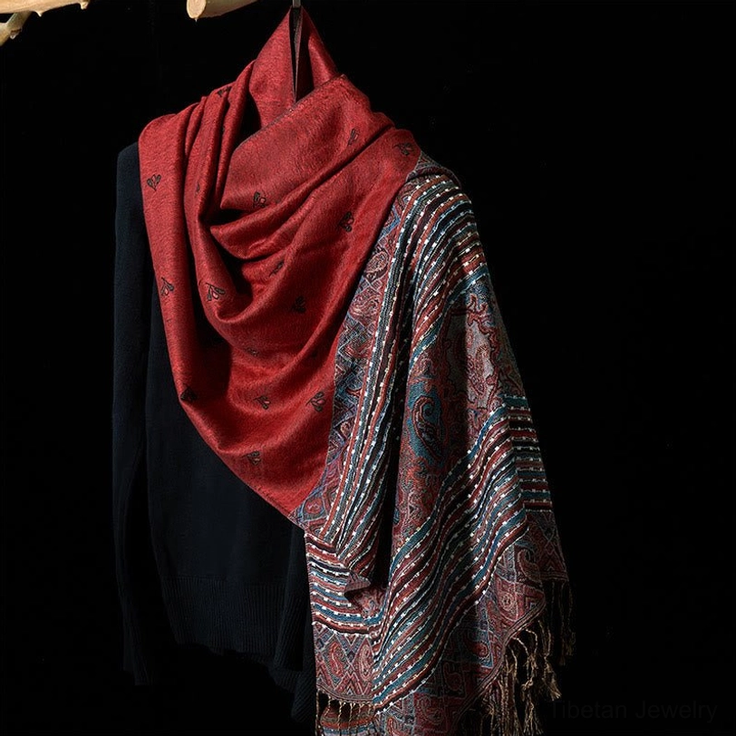 Tibetan paisley tassel shawl in FireBrick red with geometric stripe pattern, draped on black knit top - oblique hanging view showing solid color and patterned sections