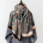 Tibetan ethnic paisley shawl with tassels draped on mannequin with grey wool coat, showing front three-quarter view of reversible geometric pattern