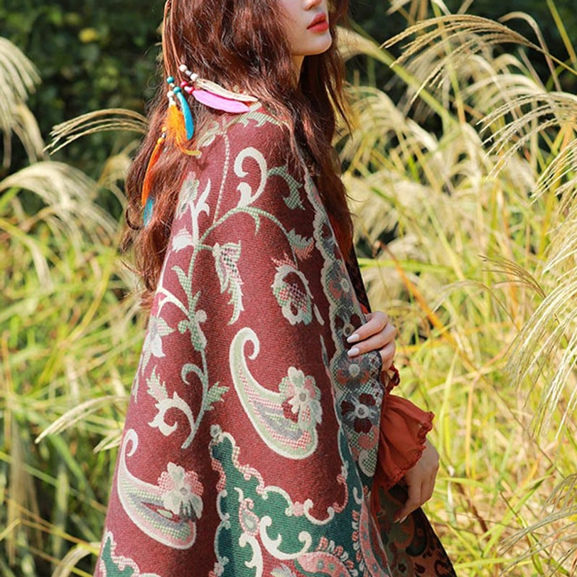 Back three-quarter view of maroon Tibetan ethnic paisley shawl in reed grass field, showing woven jacquard texture and colorful hair ornaments