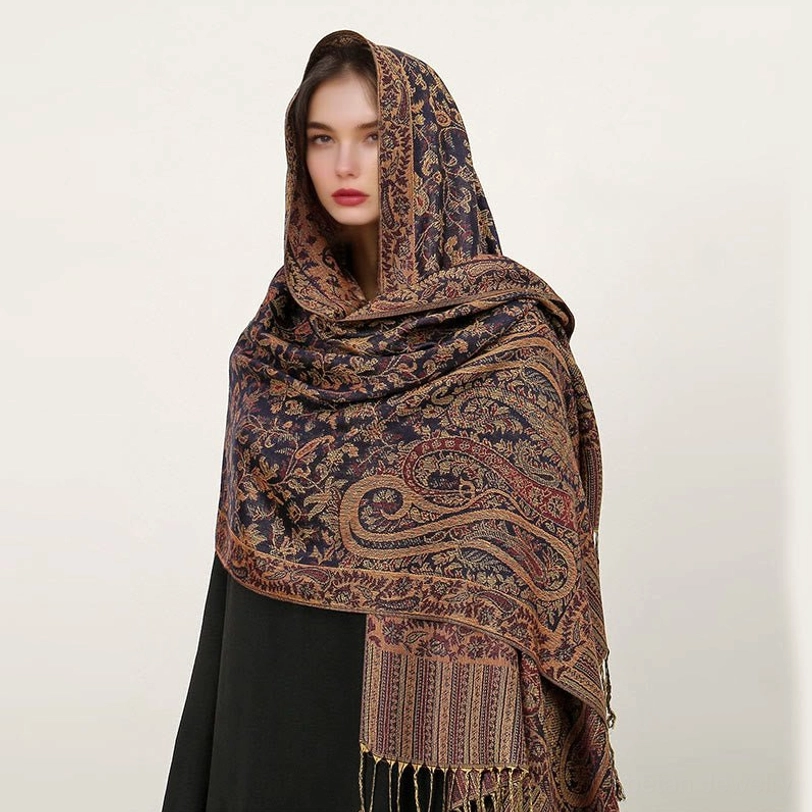 Model wearing dark navy Tibetan paisley shawl with golden brown jacquard patterns and tassel hem, front headshot view