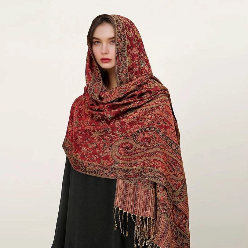 Model wearing reddish brown Tibetan paisley shawl with orange-red jacquard patterns and tassel fringe, front view