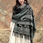 Tibetan paisley tassel shawl in dark teal worn on-body outdoors, showing front wrap style with mountain landscape background