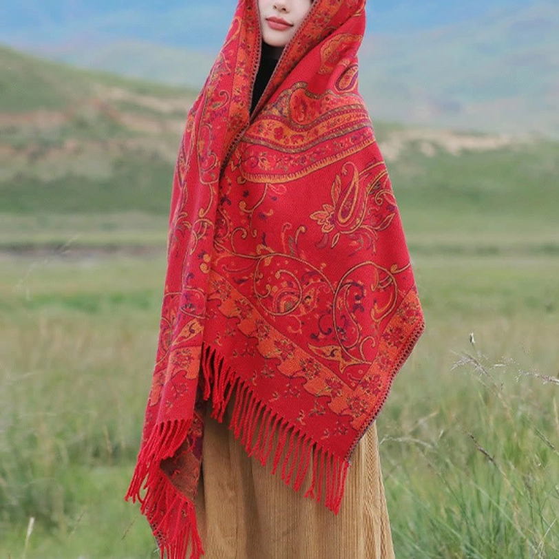 Red Tibetan paisley tassel shawl draped showing texture and long fringe hem in neutral indoor studio setting