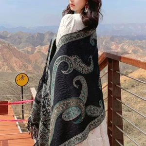 Tibetan teal paisley shawl side-back view on model at mountain overlook, displaying jacquard weave and draped fit